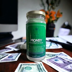 May include: A green glass jar candle with a gold lid. The label reads "Money Manifestation" and includes the text "The ultimate manifestation tool designed to attract abundance, wealth and prosperity in your life. This candle harnesses the power of natural herbs and crystals to amplify your intentions and unlock the flow of financial abundance. PalmWax Candle 16 oz."