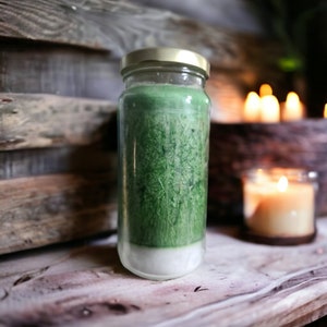 May include: A green glass jar candle with a white wax base and a gold lid. The candle is sitting on a wooden surface.