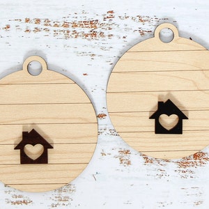 May include: Four wooden ornaments in the shape of a circle with a house design in the center. The houses have a heart in the center and are in different colors: white, black, and brown. The ornaments are perfect for decorating a home for the holidays.