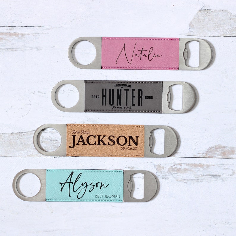 Puede incluir: Cuatro abridores de botellas personalizados con cuerpos de acero inoxidable y detalles de cuero o corcho. Los abridores est&aacute;n grabados con nombres y t&iacute;tulos, incluyendo "Natalie", "Hunter", "Jackson" y "Alyson". Fondo de madera blanca.
