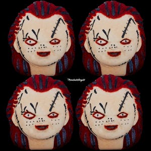 May include: Four identical bath bombs shaped like a doll head with pale skin, red hair, and black stitched facial details. Each doll head features red eyes, a wide smile, and dark freckles. The text Minibubblingbb is visible in the center.