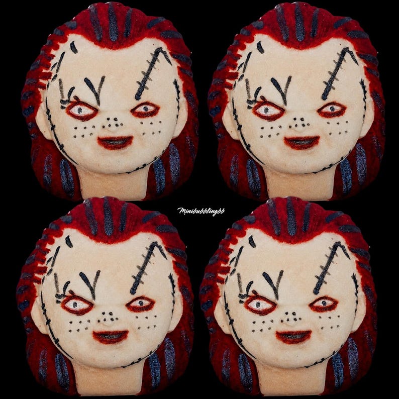 May include: Four identical bath bombs shaped like a doll head with pale skin, red hair, and black stitched facial details. Each doll head features red eyes, a wide smile, and dark freckles. The text Minibubblingbb is visible in the center.