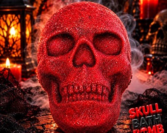 May include: A bright red, glitter-covered skull-shaped bath bomb. The surface of the skull is textured with fine, sparkling red particles. In the bottom right corner, the text reads SKULL BATH BOMB in a stylized, dripping red and black font.