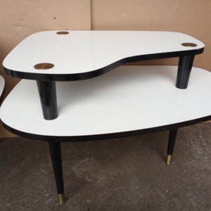May include: Two white nesting tables with black legs and gold accents. The tables have a unique, asymmetrical shape.