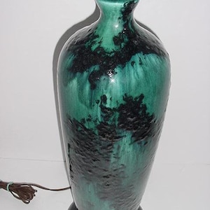 May include: A tall, ceramic table lamp with a green and black glaze. The lamp has a rounded base and a slender, vase-like body. The lamp's shade is not visible in the image.