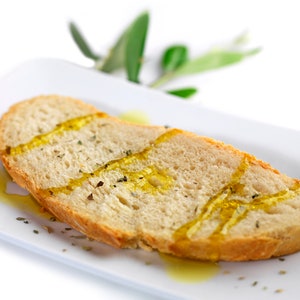 May include: A slice of crusty bread drizzled with olive oil and herbs on a white plate.