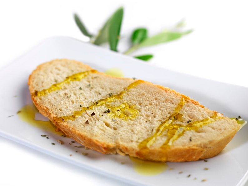 May include: A slice of crusty bread drizzled with olive oil and herbs on a white plate.
