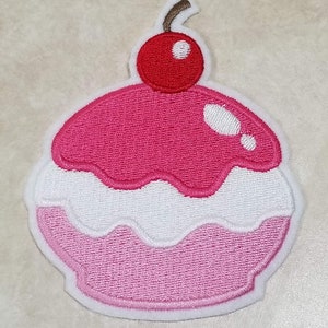 May include: Pink and white embroidered cupcake patch with a red cherry on top.