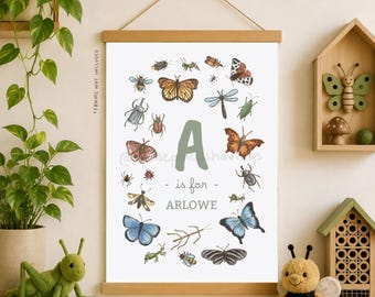 May include: A framed print featuring an illustrated alphabet with insects. The letter "A" is surrounded by various bugs and butterflies. The text "A is for Arlowe" is below the letter. The print is displayed with a wooden frame and hanging string.