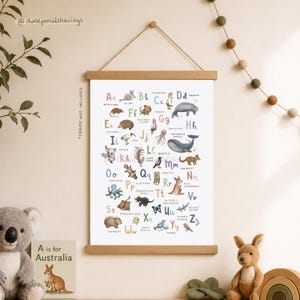 May include: A framed educational poster featuring an Australian animal alphabet. The poster displays colorful illustrations of animals like koalas, kangaroos, and wombats, each paired with a letter of the alphabet. The poster is suspended by a wooden frame.