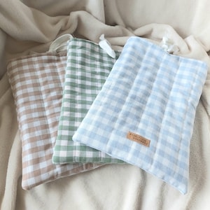Può includere: Tre pochette in tessuto a fantasia gingham. Le pochette sono nelle tonalità del beige, del verde e dell'azzurro. Ogni pochette ha un piccolo anello nella parte superiore. La pochette azzurra ha una piccola etichetta in pelle con la scritta "PEARLY DUE HANDMADE".