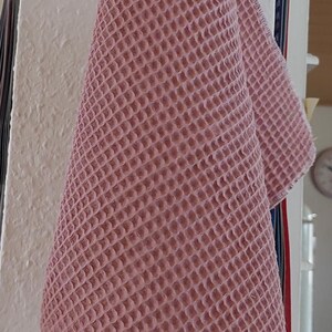 K&ouml;nnte beinhalten: Ein rosa Waffelgewebe-K&uuml;chenhandtuch h&auml;ngt an einem Holzast mit schwarzen Haken.