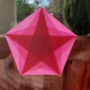 Könnte beinhalten: Ein rosa Papierstern mit fünf Zacken, gefaltet zu einer dreidimensionalen Form. Der Stern ist durchscheinend und scheint aus Seidenpapier zu sein.