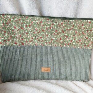 May include: A rectangular zippered pouch featuring a top section of green fabric with a small red and white floral pattern and a bottom section of sage green corduroy fabric. A small rectangular tan label with text is centered on the corduroy.