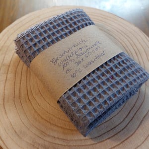 K&ouml;nnte beinhalten: Ein graues Waffeltuch aus 100% Baumwolle. Das Tuch ist ca. 30 x 50 cm gro&szlig; und bei 40 Grad Celsius waschbar. Der Text auf dem Etikett lautet "Geschirrtuch Waffel Piqu&eacute; 100% Baumwolle ca. 30x 50 cm 40&deg;C waschbar".