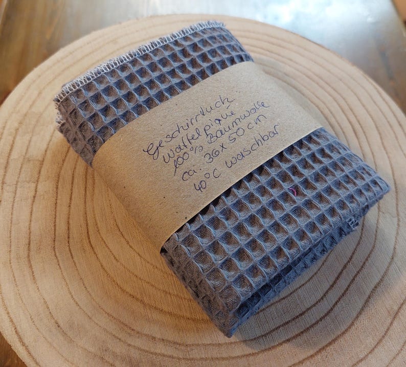 K&ouml;nnte beinhalten: Ein graues Waffeltuch aus 100% Baumwolle. Das Tuch ist ca. 30 x 50 cm gro&szlig; und bei 40 Grad Celsius waschbar. Der Text auf dem Etikett lautet "Geschirrtuch Waffel Piqu&eacute; 100% Baumwolle ca. 30x 50 cm 40&deg;C waschbar".