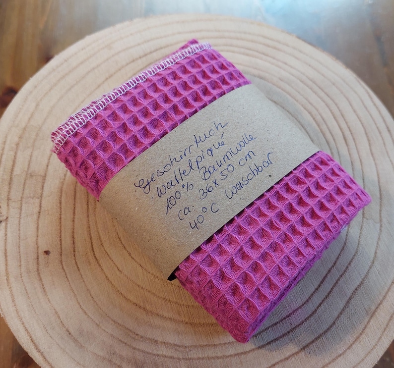 K&ouml;nnte beinhalten: Ein pinkfarbenes Waffeltuch aus 100% Baumwolle. Das Tuch ist mit "Geschirrtuch, Waffel Piqu&eacute;, 100% Baumwolle, ca. 36x 50 cm, 40&deg;C waschbar" beschriftet.