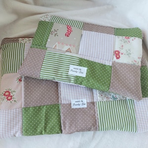 Könnte beinhalten: Zwei Patchwork-Kissen mit verschiedenen Stoffmustern, darunter Streifen, Tupfen und Blumendrucke in Grün-, Rosa- und Brauntönen. Die Kissen haben ein Etikett mit der Aufschrift "made by Pearly-Sue".
