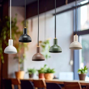 May include: Five pendant lights in a row, each with a rounded, downward-facing shade. The shades are in white, black, brown, green, and off-white. The cords are black or white, and the fixtures have gold-colored accents. The lights hang above a wooden table.