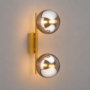 May include: A wall-mounted light fixture featuring a vertical yellow metal bar attached to a rectangular yellow base. Two spherical, semi-transparent smoked glass globes are mounted on the bar, each containing a glowing light bulb inside.