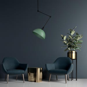 Puede incluir: Escena de diseño de interiores con dos sillones verde azulado, una mesa auxiliar dorada y una planta alta en una maceta dorada. Una lámpara verde en forma de cúpula cuelga del techo. El fondo es una pared azul oscuro.