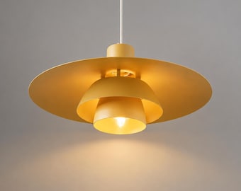Pode incluir: Uma luminária pendente amarelo-mostarda com uma cúpula circular larga e plana sobreposta a uma cúpula interna menor em forma de domo. A lâmpada está suspensa por um fio branco e emite uma luz quente voltada para baixo.
