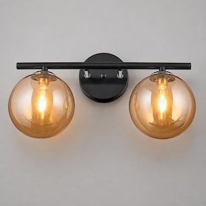 May include: A wall-mounted light fixture featuring a horizontal matte black metal bar attached to a circular black base. Two spherical, amber-tinted glass globes are suspended from the bar, each housing a glowing light bulb inside.