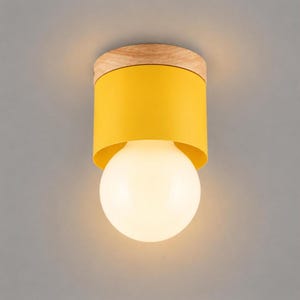 May include: A flush mount ceiling light fitting featuring a cylindrical yellow metal shade attached to a light-toned wooden base. A large, spherical, frosted white glass light bulb extends from the centre of the yellow metal cylinder.