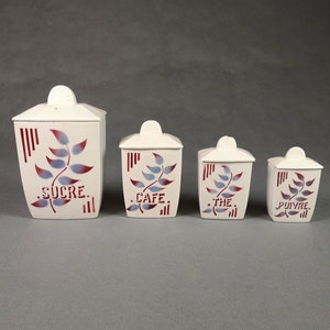 Peut inclure: Ensemble de quatre pots en céramique blanche avec des motifs de feuilles rouges et bleues. Les pots sont étiquetés "SUCRE", "CAFE", "THE" et "POIVRE".
