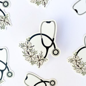 May include: Multiple black and white stickers featuring a stethoscope with white flowers around it. The stickers are on a white background.