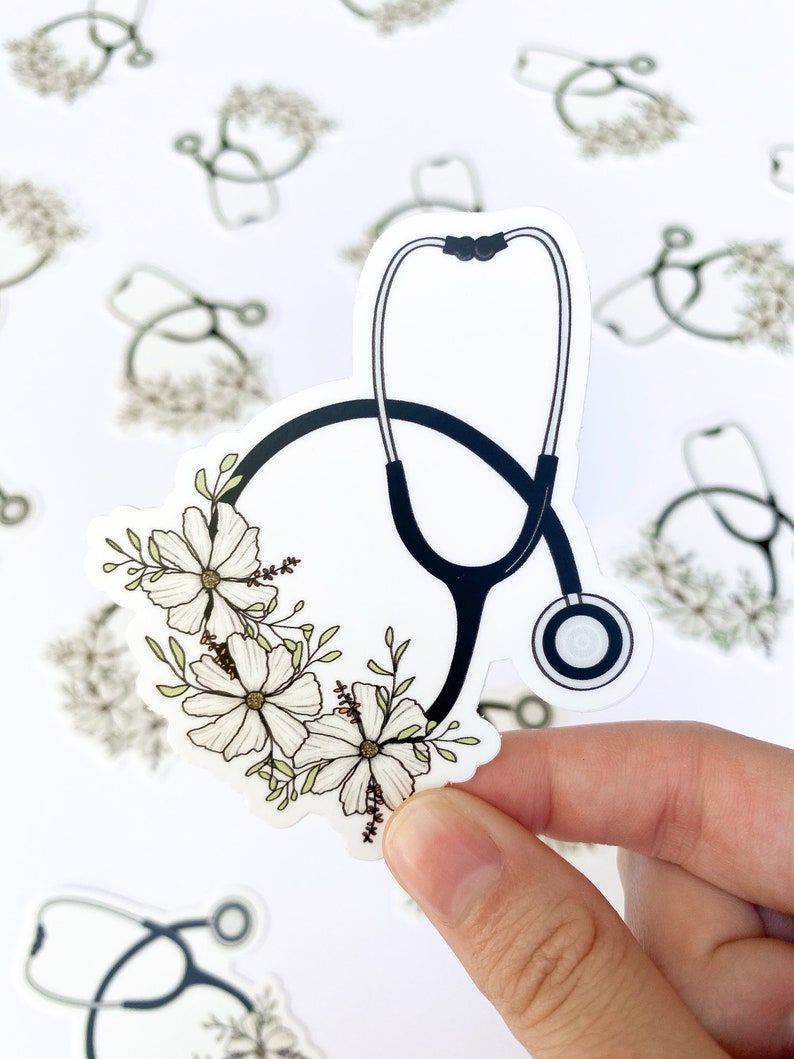 May include: A white sticker with a black stethoscope and white flowers. The stethoscope has a black tube and a silver listening piece. The flowers are arranged in a circle around the stethoscope.
