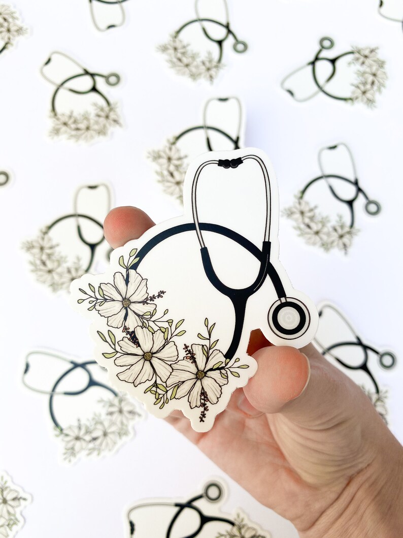 May include: A white sticker with a black stethoscope and white flowers. The stethoscope is in the shape of a circle with the earpieces at the top. The flowers are arranged around the stethoscope.