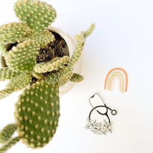 May include: A sticker featuring a black stethoscope with white flowers around it. A rainbow sticker with orange, peach, and green colors is also in the image.