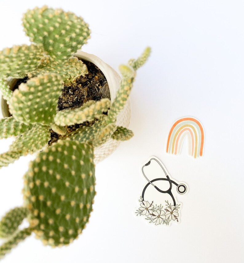 May include: A sticker featuring a black stethoscope with white flowers around it. A rainbow sticker with orange, peach, and green colors is also in the image.