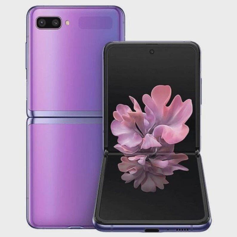 Puede incluir: Dos tel&eacute;fonos Samsung Galaxy Z Flip morados. Uno est&aacute; cerrado, mostrando una superficie lisa y reflectante. El otro est&aacute; abierto, mostrando una pantalla negra con un gr&aacute;fico floral rosa. Los tel&eacute;fonos tienen un dise&ntilde;o elegante y moderno.