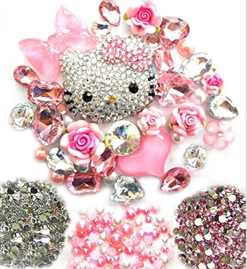 Puede incluir: Un surtido de adornos decorativos con una cara de gato cubierta de brillantes pedrer&iacute;a, rosas rosas y varias formas de cristal rosa y transparente. El arreglo incluye un lazo rosa, un coraz&oacute;n y grupos de cuentas rosas y plateadas.