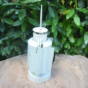 May include: A white metal lantern with a handle and a hinged door. The lantern has a rounded shape and a smooth surface.