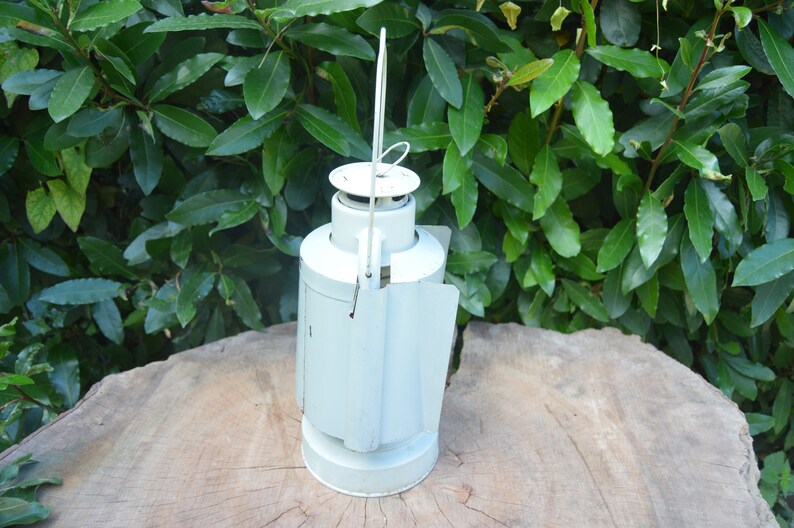 May include: A white metal lantern with a handle and a hinged door. The lantern has a rounded shape and a smooth surface.