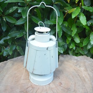 May include: A white metal lantern with a handle and a round top. The lantern is sitting on a wooden surface.