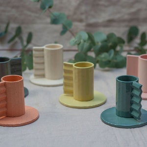 May include: Set of six ceramic cups with unique, textured handles. The cups are in various colors, including pink, green, yellow, and orange. Each cup has a matching saucer.
