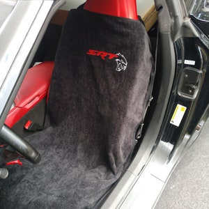 Puede incluir: Una funda de toalla negra para asiento de coche colocada sobre un asiento de vehículo de cuero rojo. La funda presenta el texto SRT bordado en rojo y un logotipo de cabeza de gato bordado en blanco en la parte superior de la tela.
