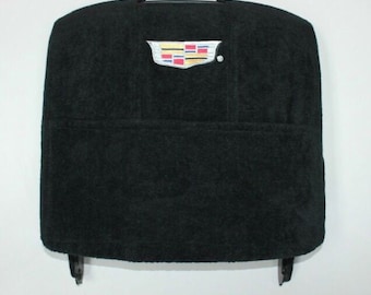 Op de afbeelding: Een zwarte rechthoekige hoofdsteunhoes met een textieloppervlak met textuur. In het midden bovenaan bevindt zich een geborduurd Cadillac-logo met een schild in rode, blauwe, gele en zwarte segmenten, samen met een klein zilverkleurig metalen accent.