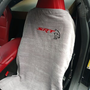 Könnte beinhalten: Ein hellgrauer Handtuch-Sitzbezug, der über einen roten Autositz drapiert ist. Der Bezug zeigt den roten Schriftzug SRT und ein schwarzes, gesticktes Katzenkopf-Logo in der Mitte. Der Stoff hat eine weiche, strukturierte Optik und bedeckt die Rückenlehne.