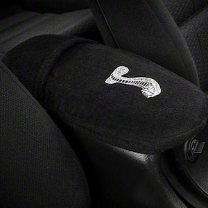 May include: Black car seat with a black armrest featuring a white embroidered snake logo.