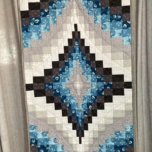 May include: A quilt with a diamond pattern in shades of blue, gray, and black. The quilt is made of squares of fabric sewn together to create a geometric design.