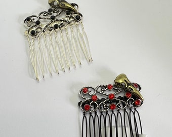 May include: Two hair combs with a decorative design featuring a bird skull and rhinestones. One comb has black rhinestones and a silver comb, the other has red rhinestones and a black comb.