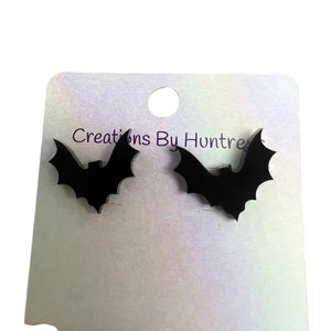 May include: A pair of black bat-shaped stud earrings on a white card with the text "Creations By Huntress".