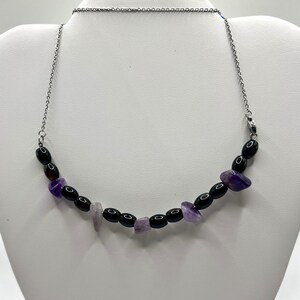 Könnte beinhalten: Eine silberne Kettenkette mit schwarzen und violetten Edelsteinperlen. Die Kette hat einen Verschluss.