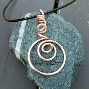 May include: A rose gold wire pendant necklace with a spiral design. The pendant is hanging from a black leather cord.