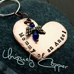 May include: Copper heart-shaped keychain with a small angel charm and blue crystal bead. The keychain is engraved with the text "Mommy of an Angel".